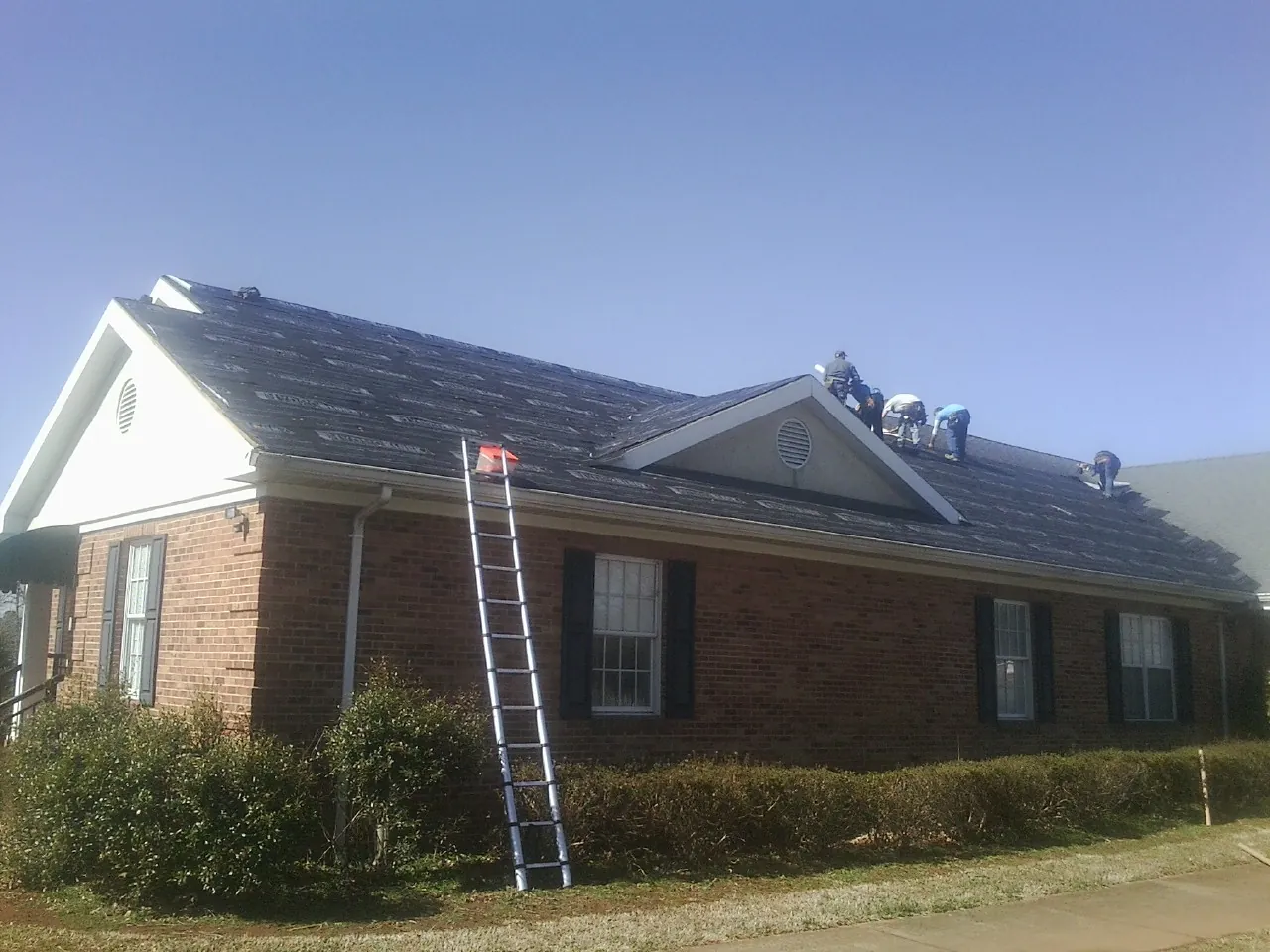 Crew tearing shingles off a brick ranch roof with a ladder set — Metal Roof Repair work by our crew in Glennville