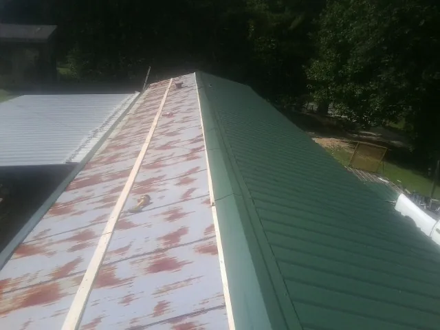 Old rusted panels beside newly installed green metal roofing — Wind Damage Roof Repair by Roofing Brothers in Glennville