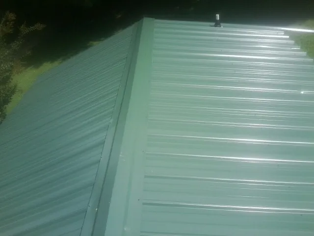 New green metal panels meeting at the ridge of a roof — Flat Roof Repair work by our crew in Glennville