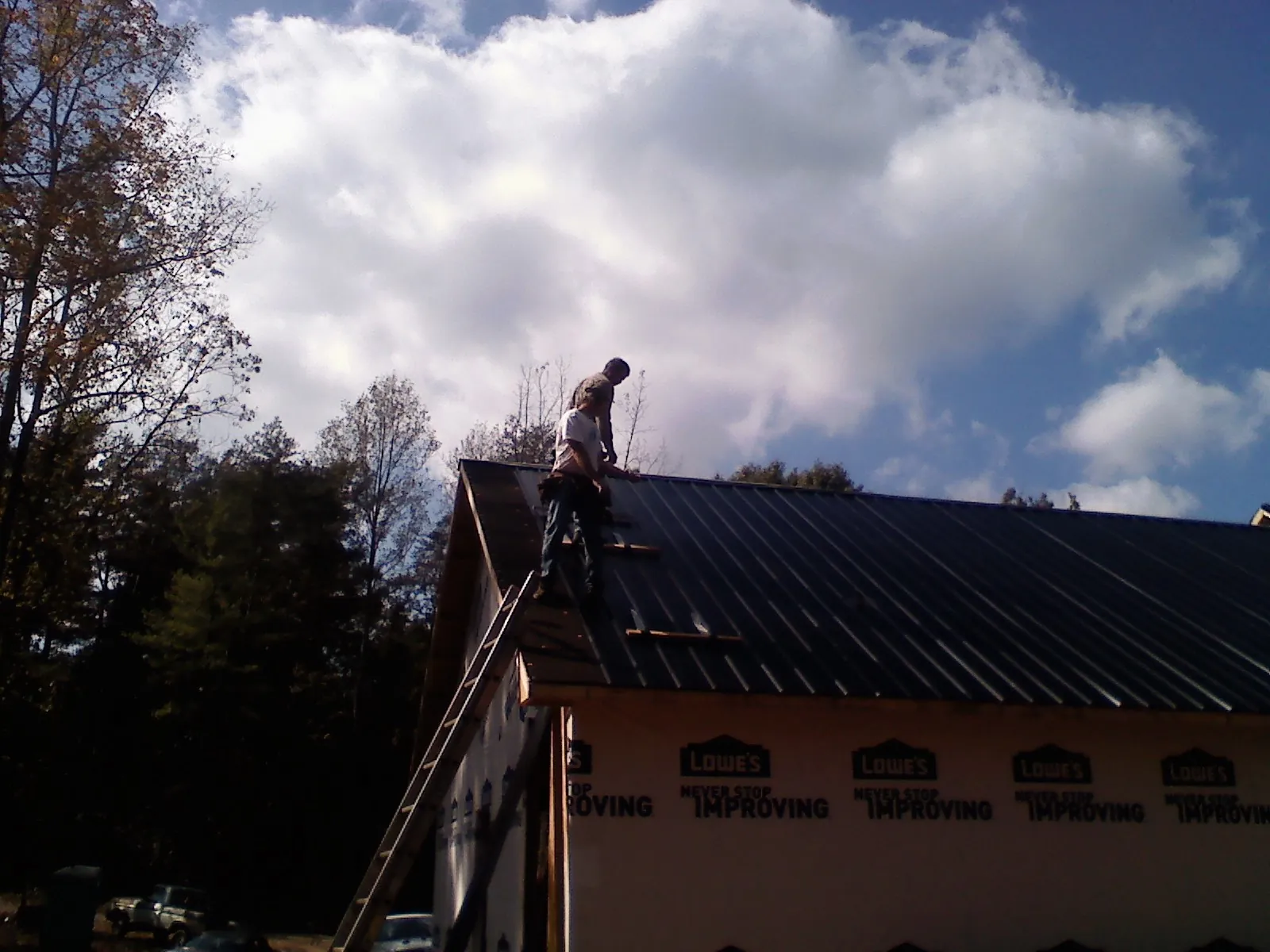Roofer fastening dark metal panels high against a cloudy sky, from a Roof Inspection job in Glennville