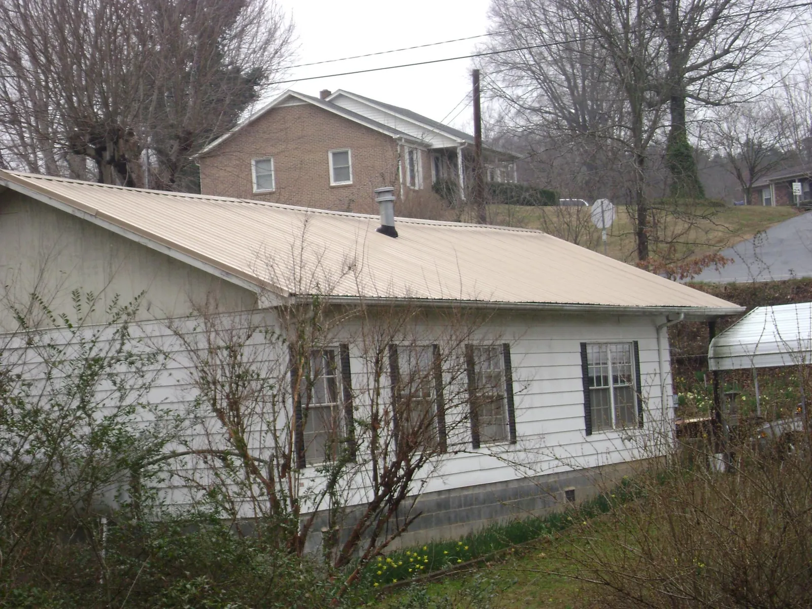 Tan metal roof on a white sided house set into a hillside — Commercial Roofing by Roofing Brothers in Glennville