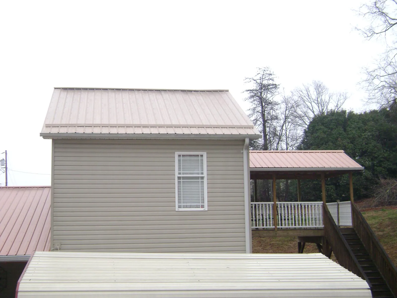 Tan metal roofs on a two story addition and attached porch, from a Roof Replacement job in Glennville